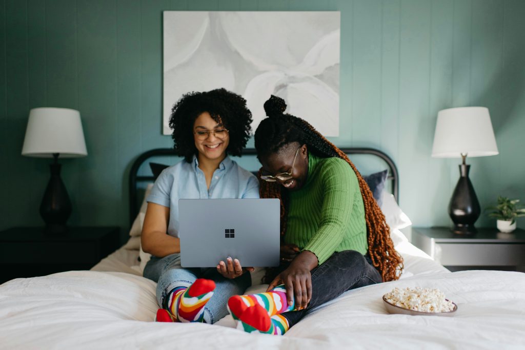 women sitting on a bed using a laptop